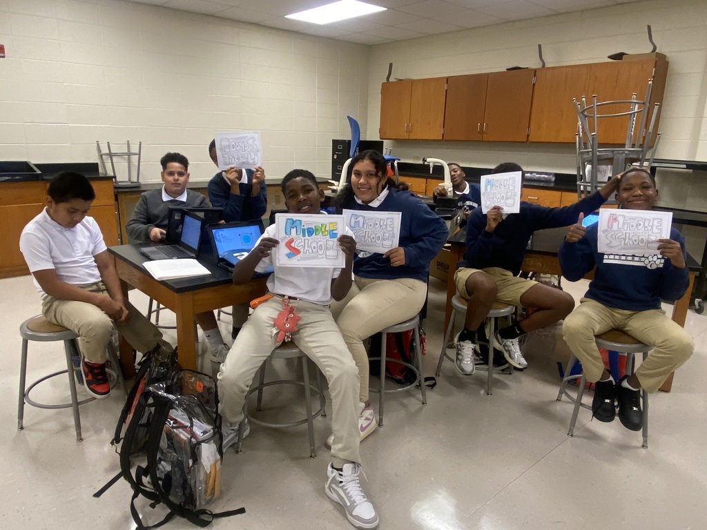 Group of students sitting at tables, holding up some work