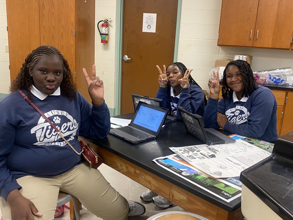3 girls sitting at a table with computers holding up peace signs
