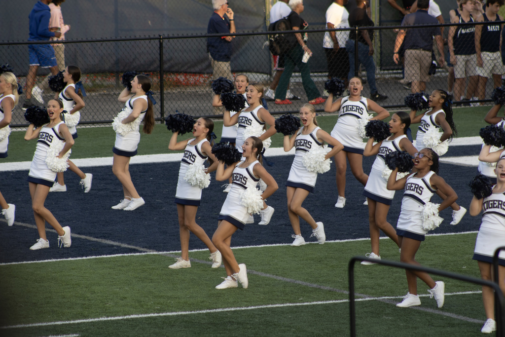 Group of girls in cheer uniforms, performing a cheer or dance on a football field