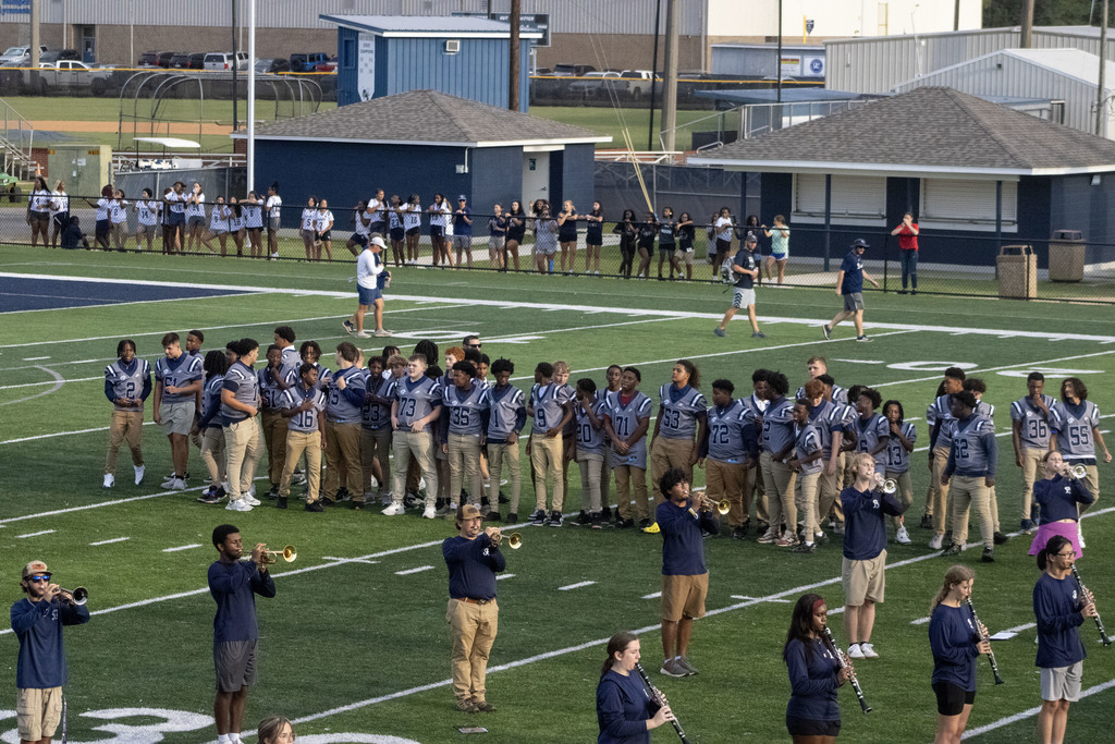 Football team on a field in gray jerseys, marching band members playing also