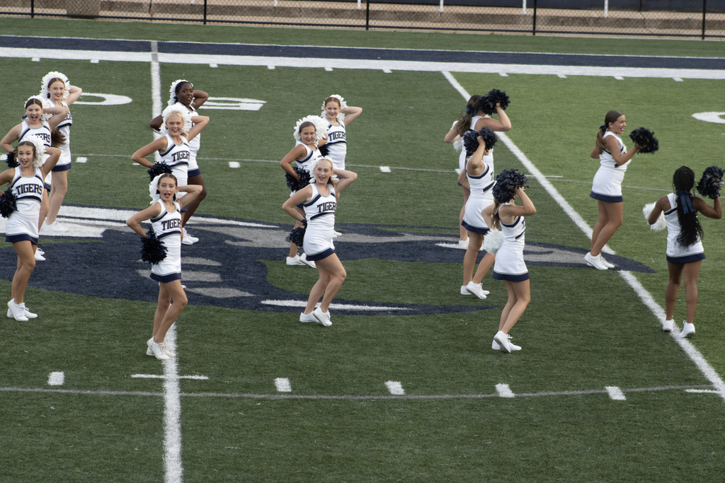 Group of girls in cheer uniforms, performing a cheer or dance on a football field