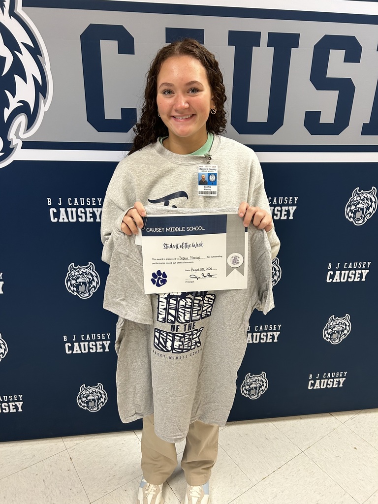 Girl standing in front of backdrop holding a certificate and t-shirt
