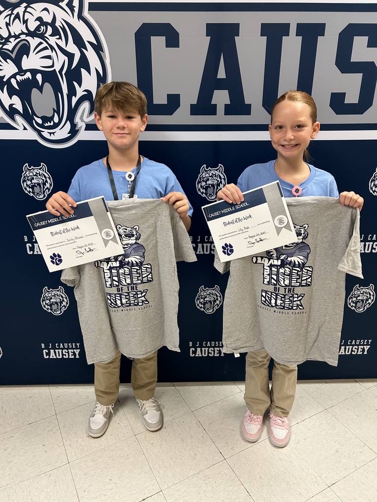 Girl and boy standing in front of backdrop holding a certificate and t-shirt