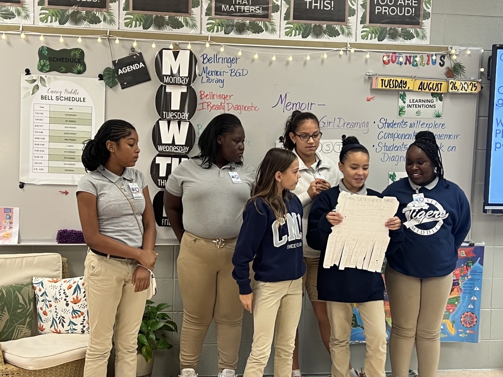 6 girls standing in front of a class. 1 holding a poster and reading something.