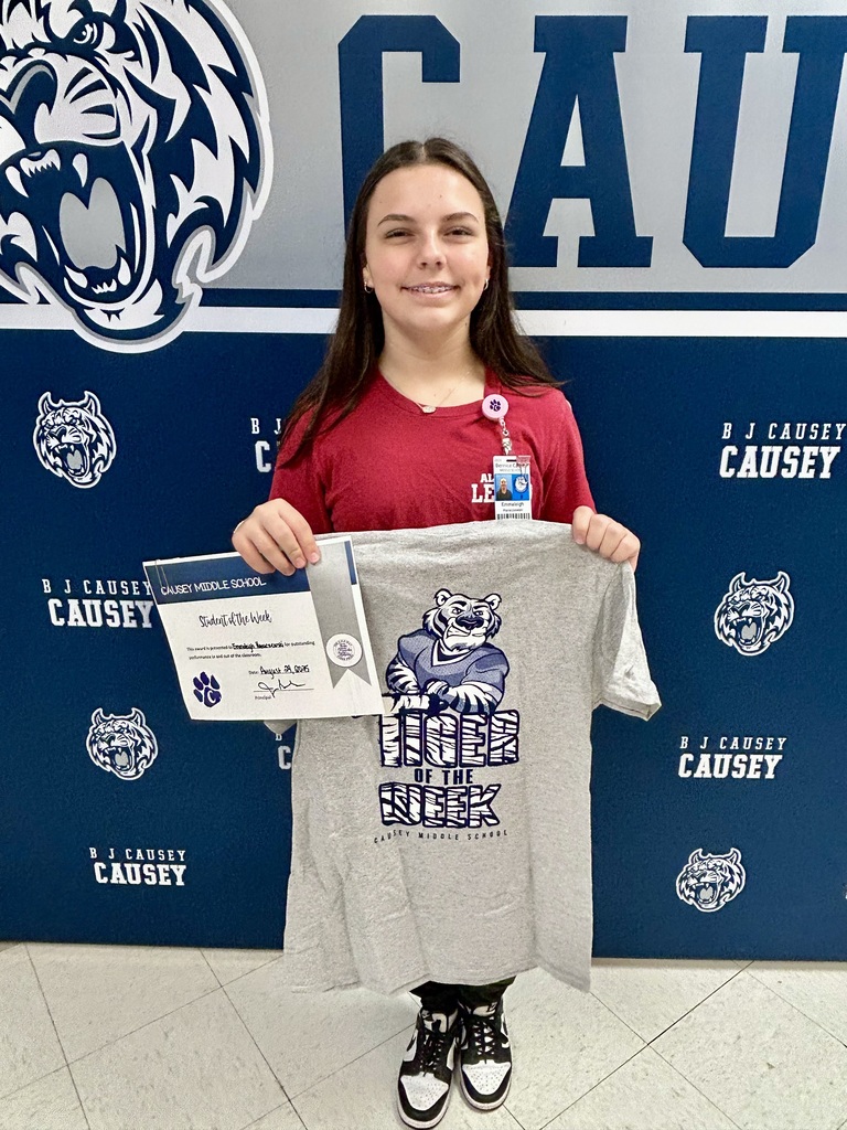 Girl standing in front of backdrop holding a certificate and t-shirt