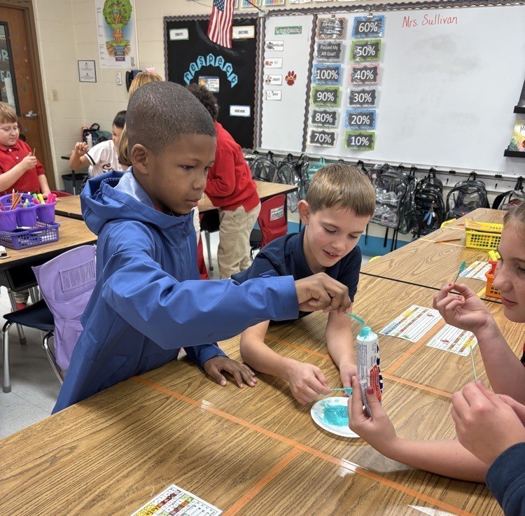 A boy dabs at a tube of toothpaste with a Q tip, while others look on
