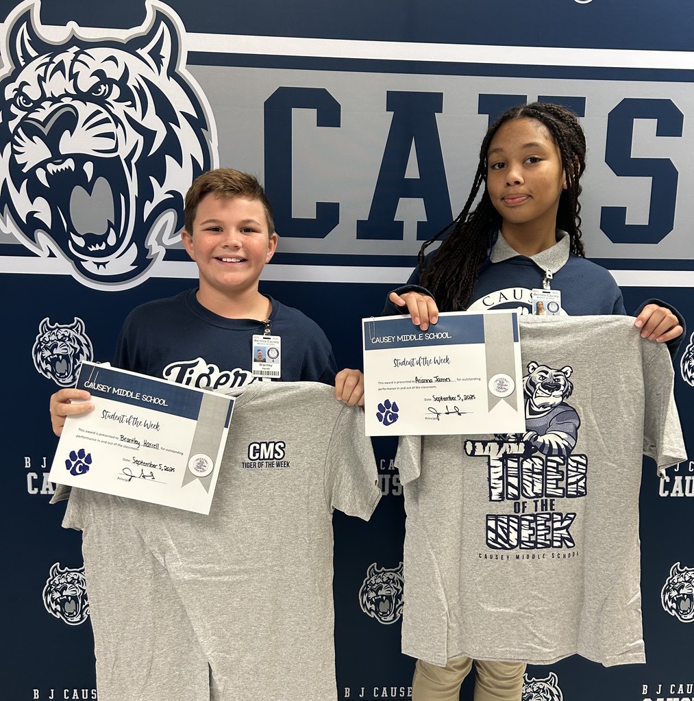 A boy and girl standing in front of a backdrop holding a t-shirt and certificate