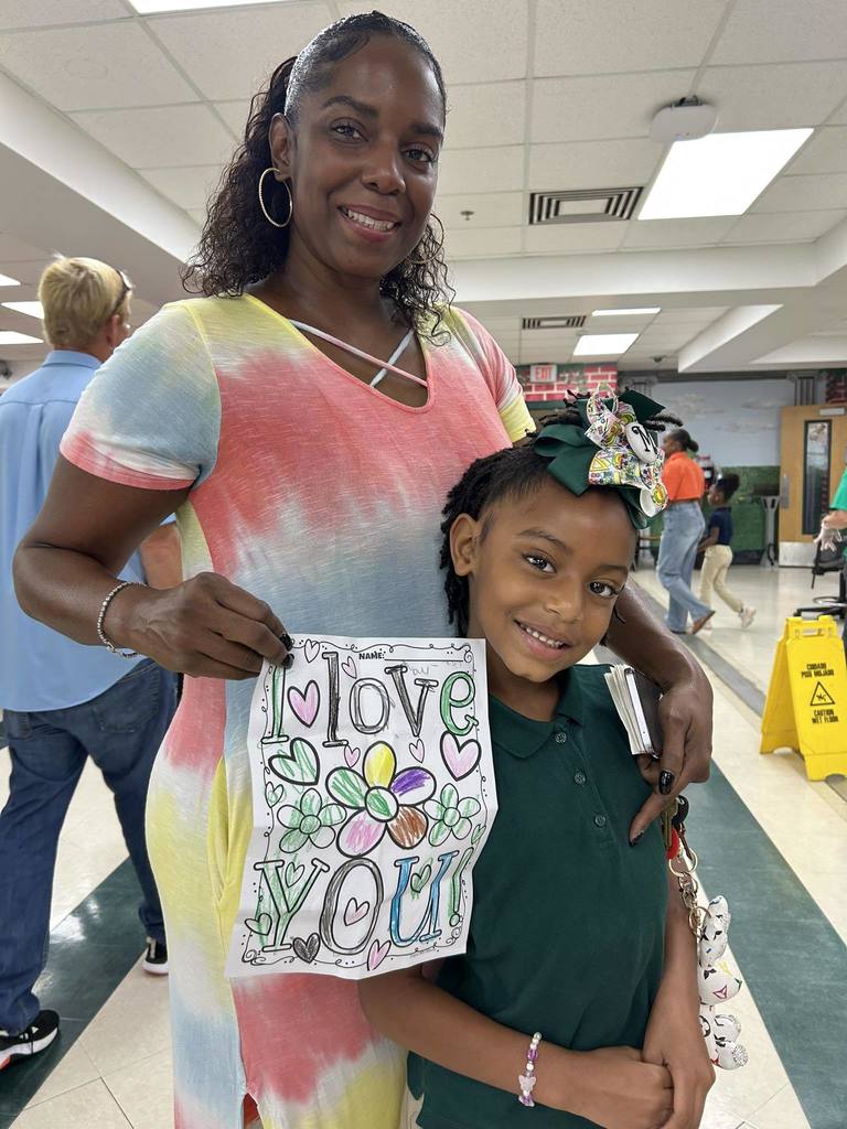 A grandmother holding a paper that says "I love you," standing with a student