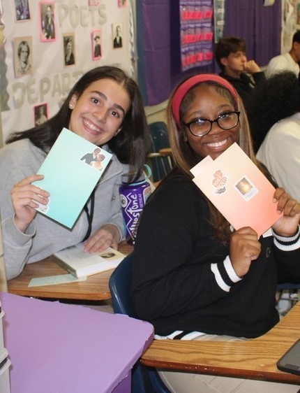 Two girls smiling and holding up their writing journals