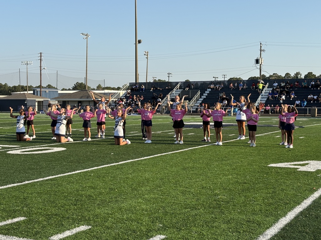 Group of cheerleaders and small girls doing a chant on a football field