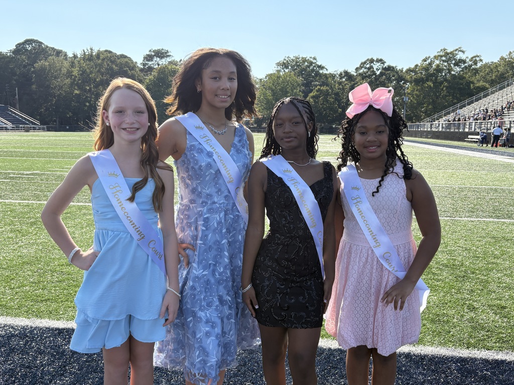 Group of 4 girls in dresses and sashes, standing on a football field