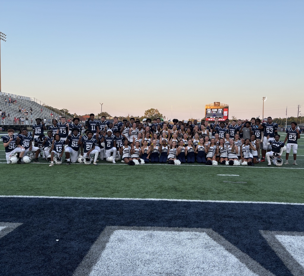 Football team, cheerleaders, and dance team on field after homecoming game with the scoreboard in the background