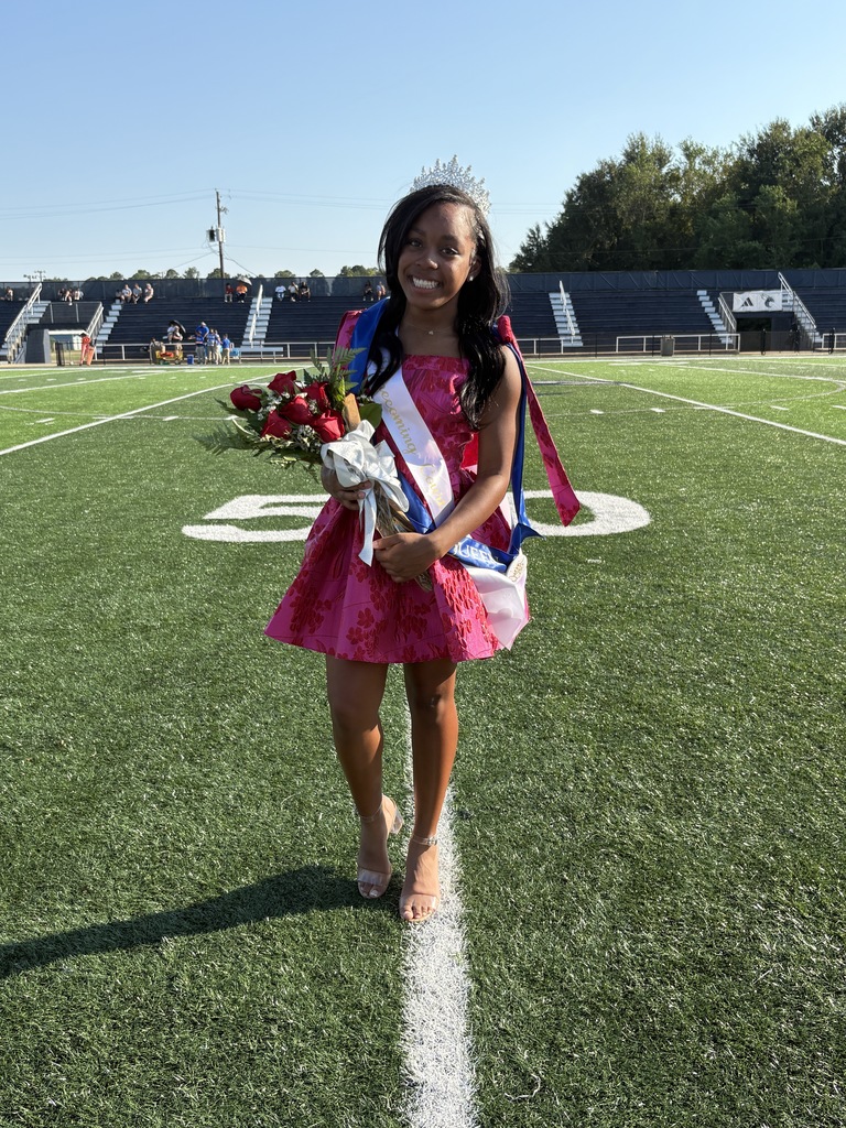 Girl in a pink dress, standing on a football field, holding flowers, wearing a sash and crown, Raegan Fincher, Homecoming Queen 2025