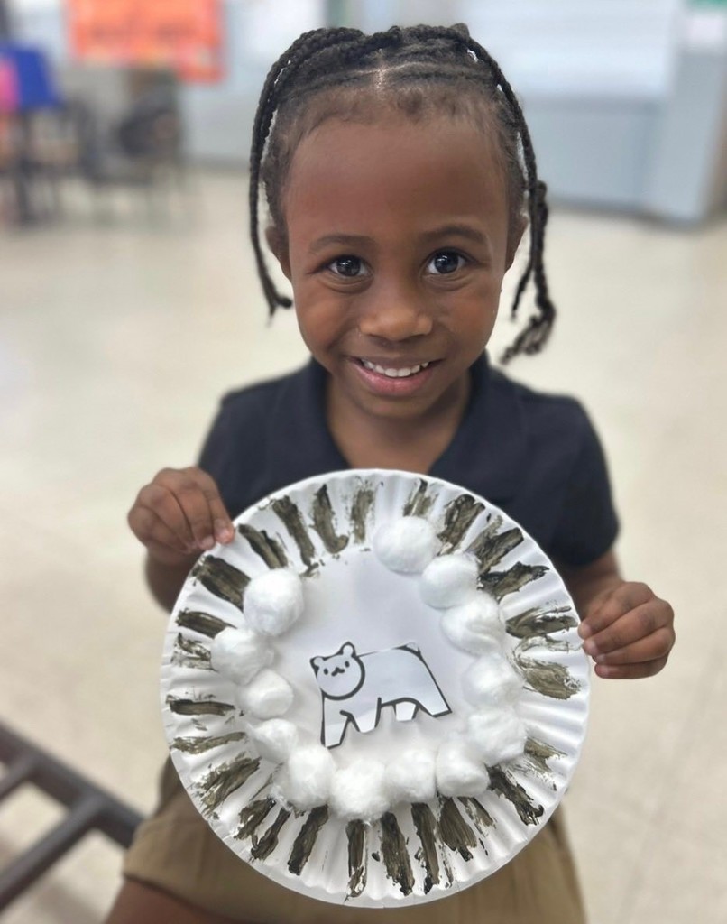 A child holds a paper plate painted with a polar bear