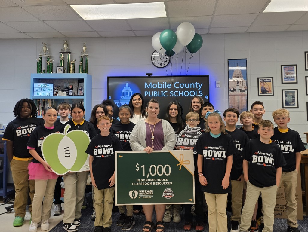 Grand Bay Middle School teacher Justine Wilson stands with her students and a sign that reads "$1,000 in Donors Choose classroom resources"