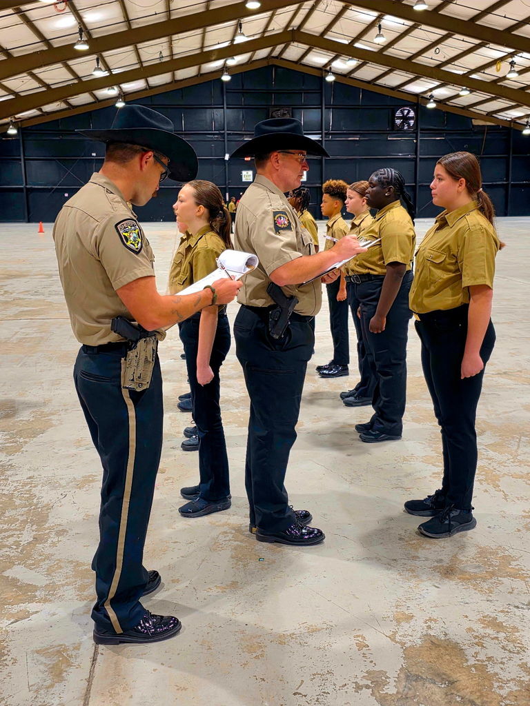 Group of cadets in uniforms and a formation being inspected by 2 men in uniform