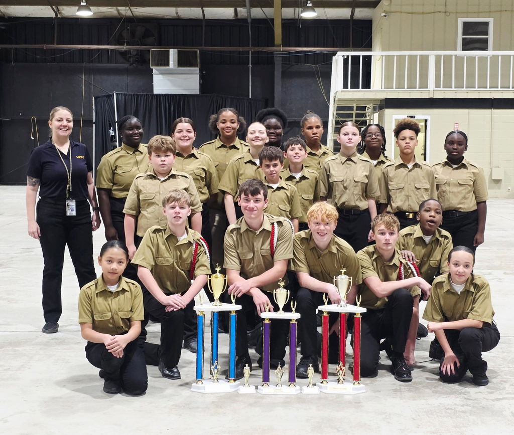 Group of students in uniforms with trophies in front of them.