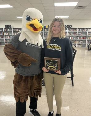 Luisa Williams holds a plaque while posing alongside the U.S. Sports University's eagle mascot