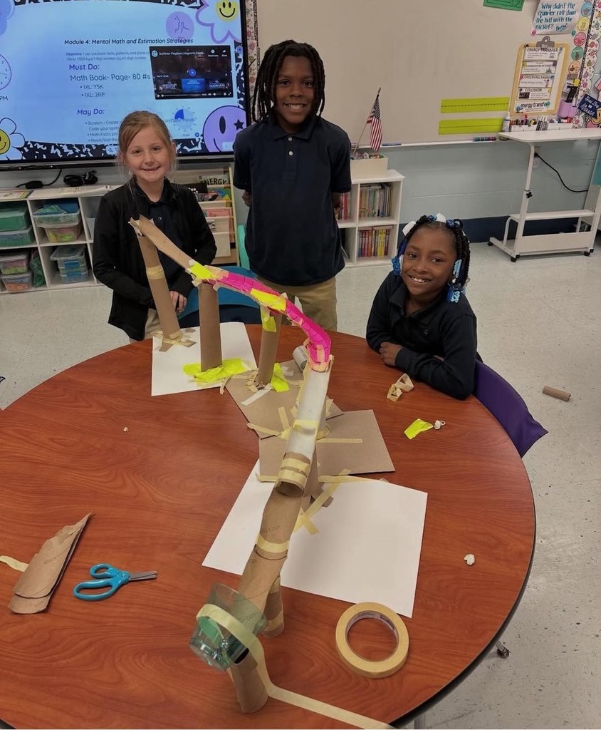 Three students with a roller coaster they built from paper towel rolls