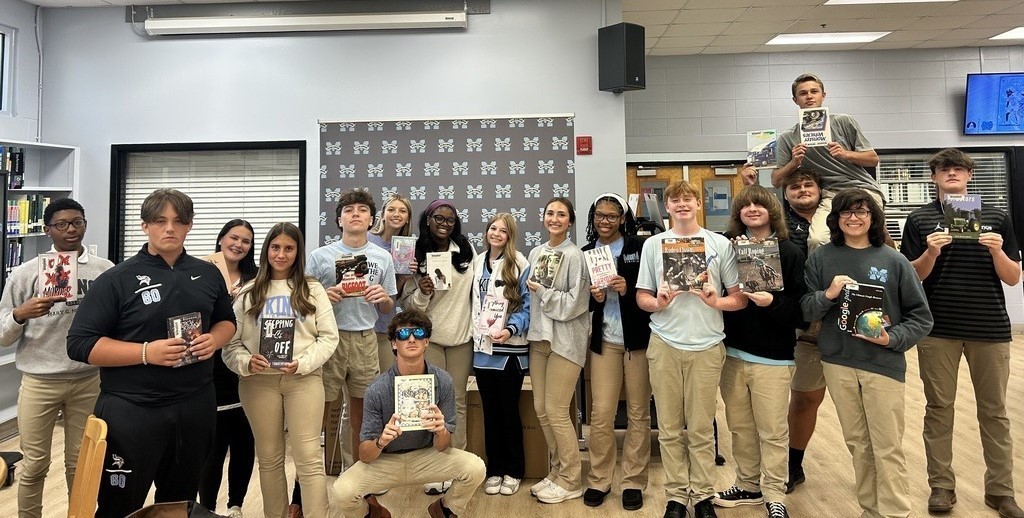 A group of high school students holding up books
