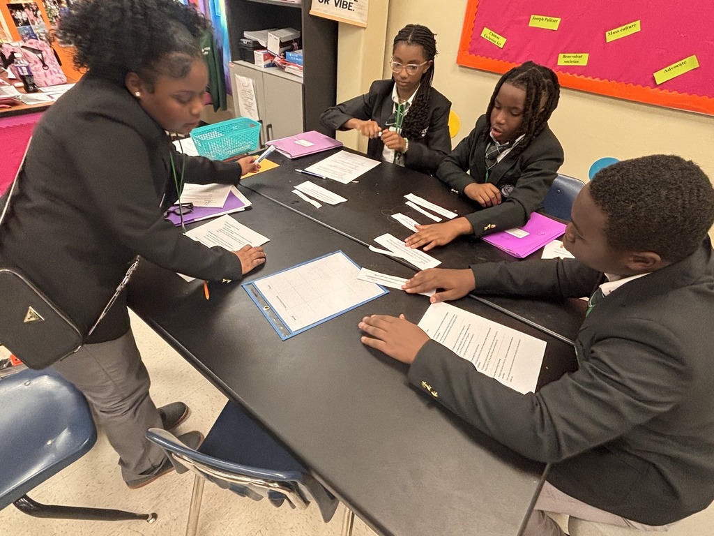 Four students sitting around a table with sheets of paper, talking
