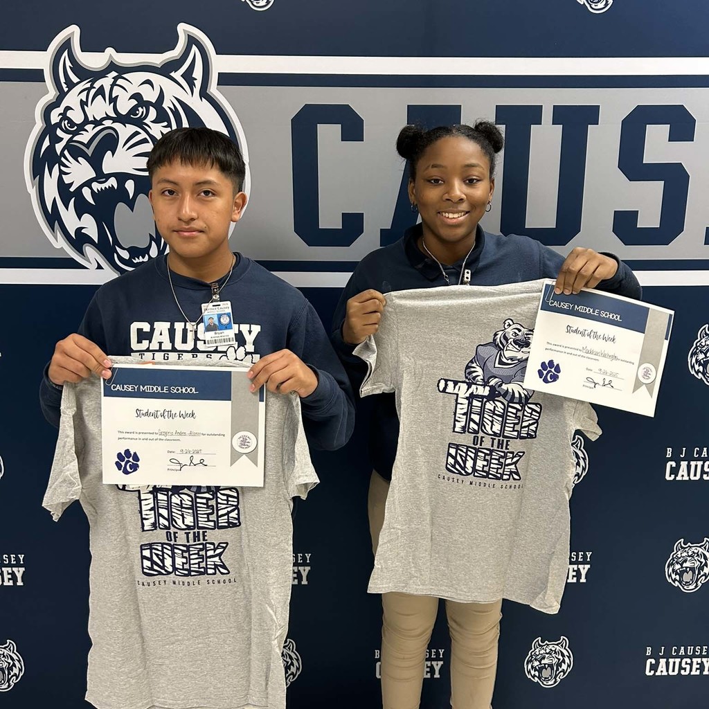 A boy and girl standing in front of a backdrop holding a t-shirt and certificate