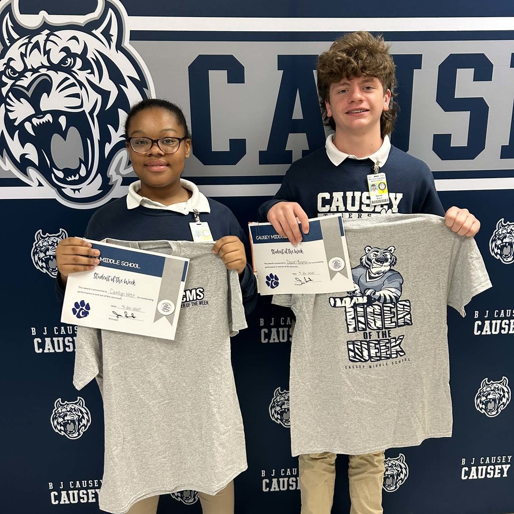 A boy and girl standing in front of a backdrop holding a t-shirt and certificate