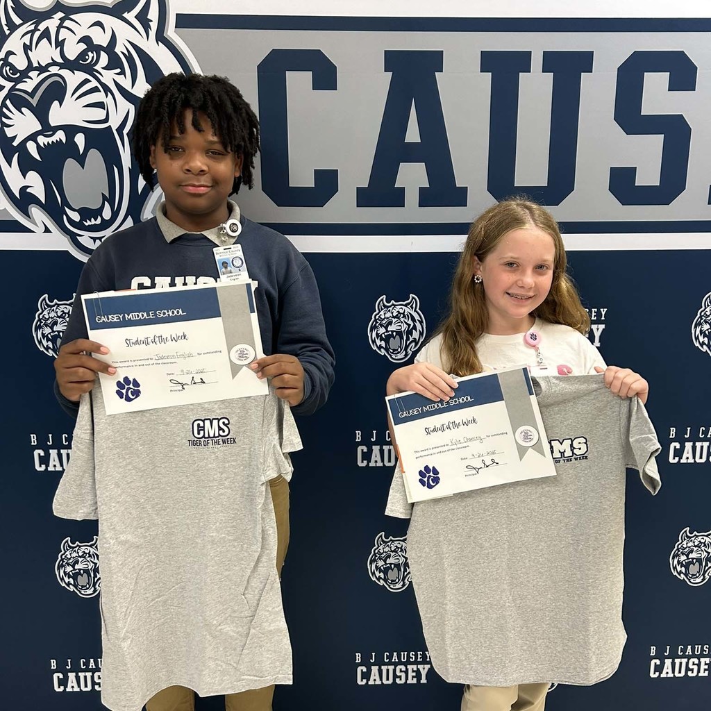 A boy and girl standing in front of a backdrop holding a t-shirt and certificate