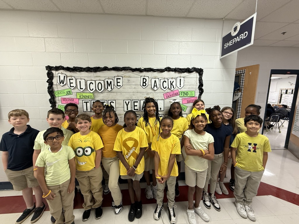 A group of students in yellow shirts standing in a hallway