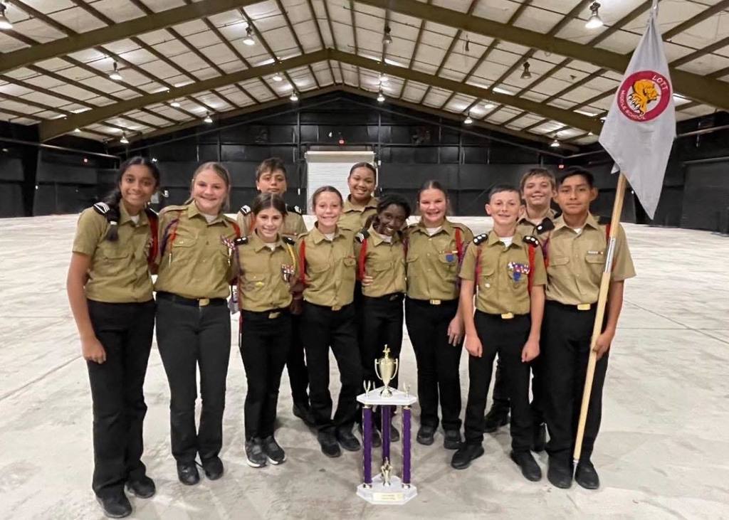 A group of middle school JROTC students in uniform, standing with a trophy