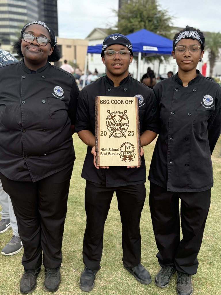 Three high school students in black culinary jackets, holding an award