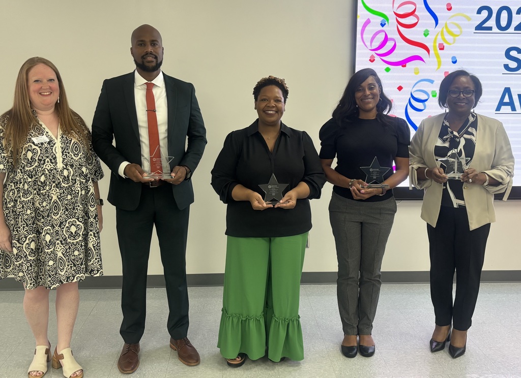 A group of five people, with four holding awards