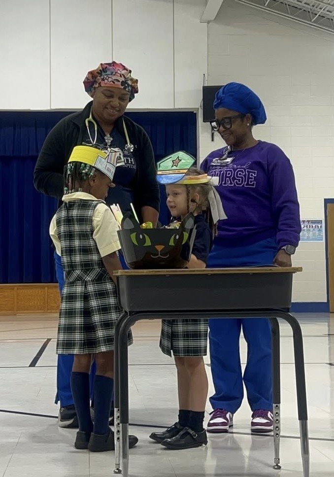 Two nurses standing with two elementary students behind a desk
