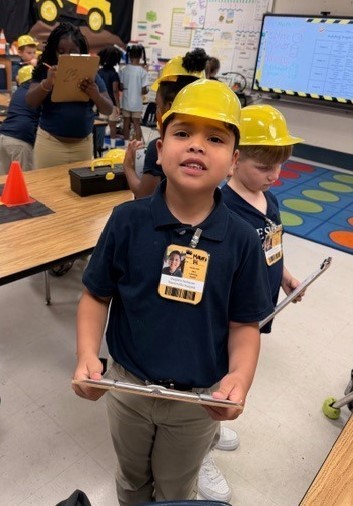 An elementary student in a hardhat holds a clipboard