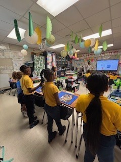 Student watch a teacher demonstration while standing at their desks.