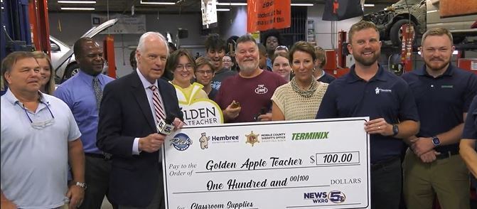A bunch of people holding a large check for $100 that reads Golden Apple Teacher