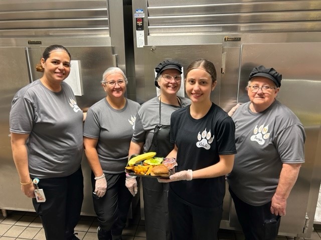 Four cafeteria workers, one of whom is holding a tray of food