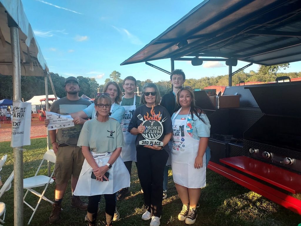 A group of students and instructors in aprons, with one holding an award for third place
