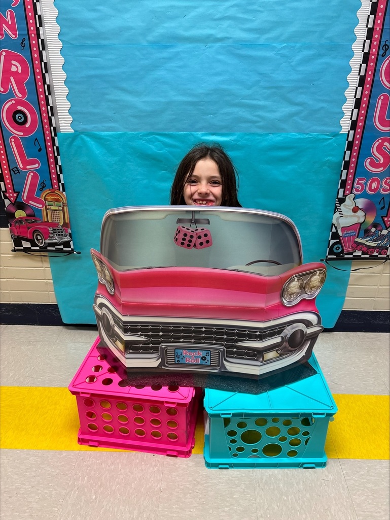 A student poses in a pink 50's classic car cardboard cutout.