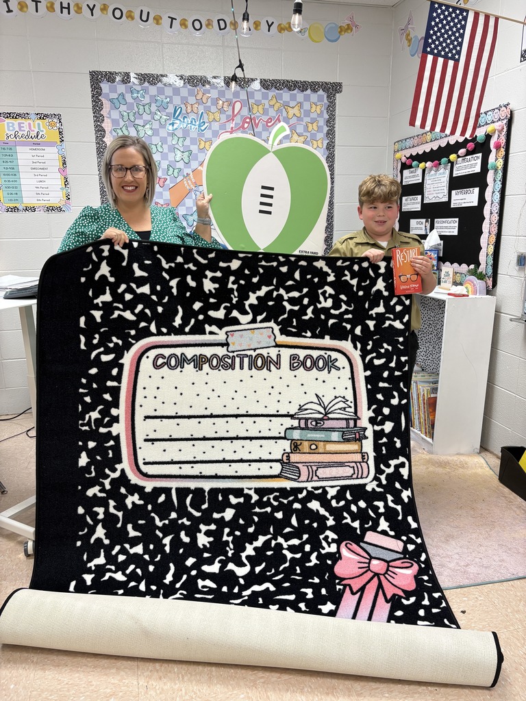 Picture of teacher and student in a classroom, holding up a new rug and book