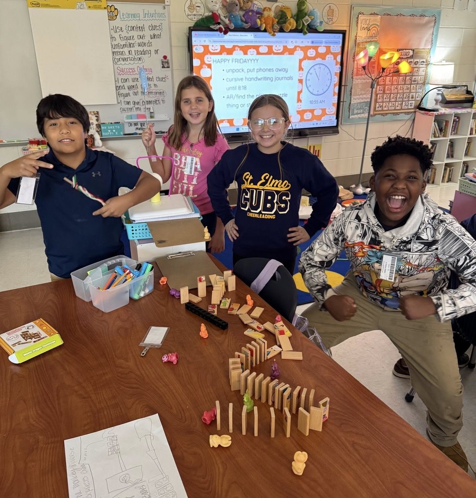 Four students smiling behind a table filled with dominoes