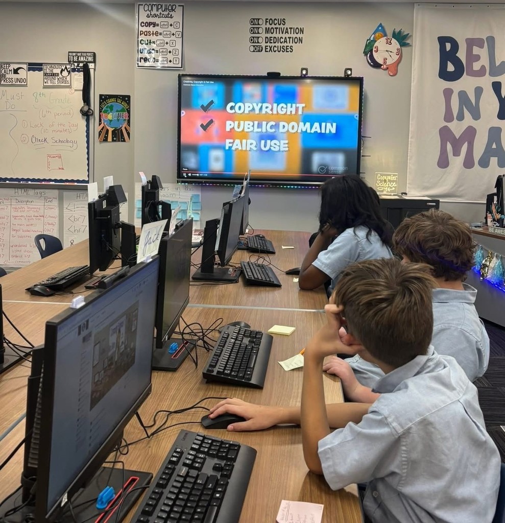 Students sit at computers and look at a smartboard, which carries the words "Copyright, public domain, fair use"