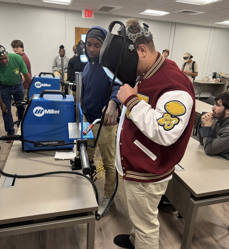 A student in a letter jacket tries on a welding mask