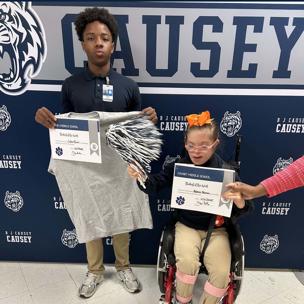 2 students holding up t-shirts and certificates