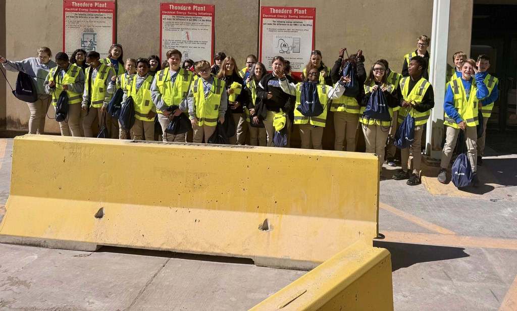 A group of students in safety vests, standing in front of a concrete barrier