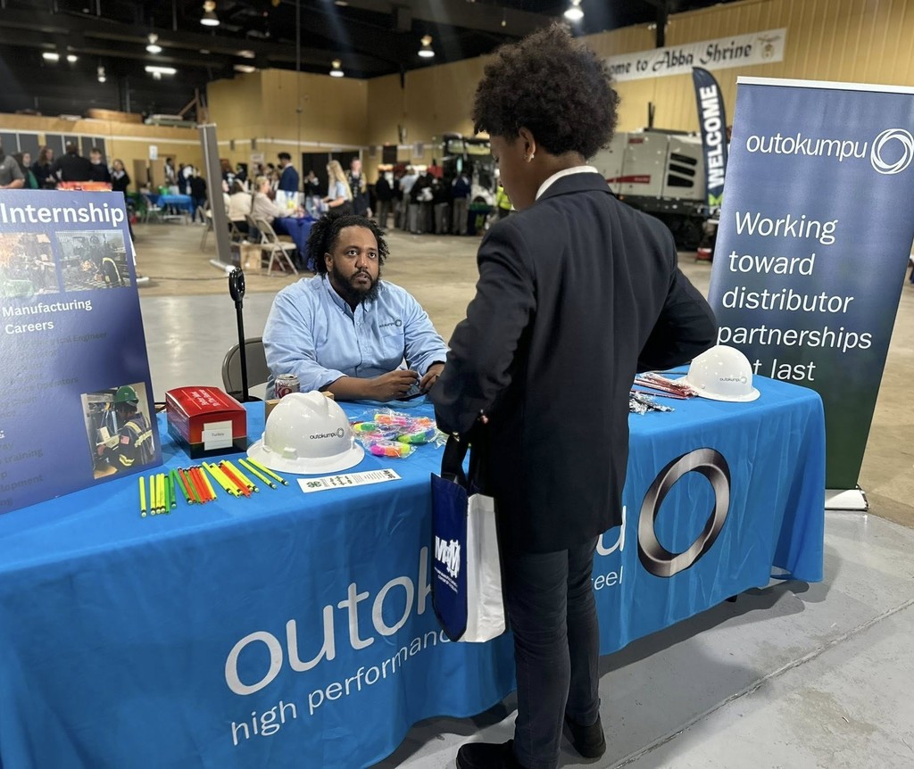 A man talks with a student at the Outokumpu table