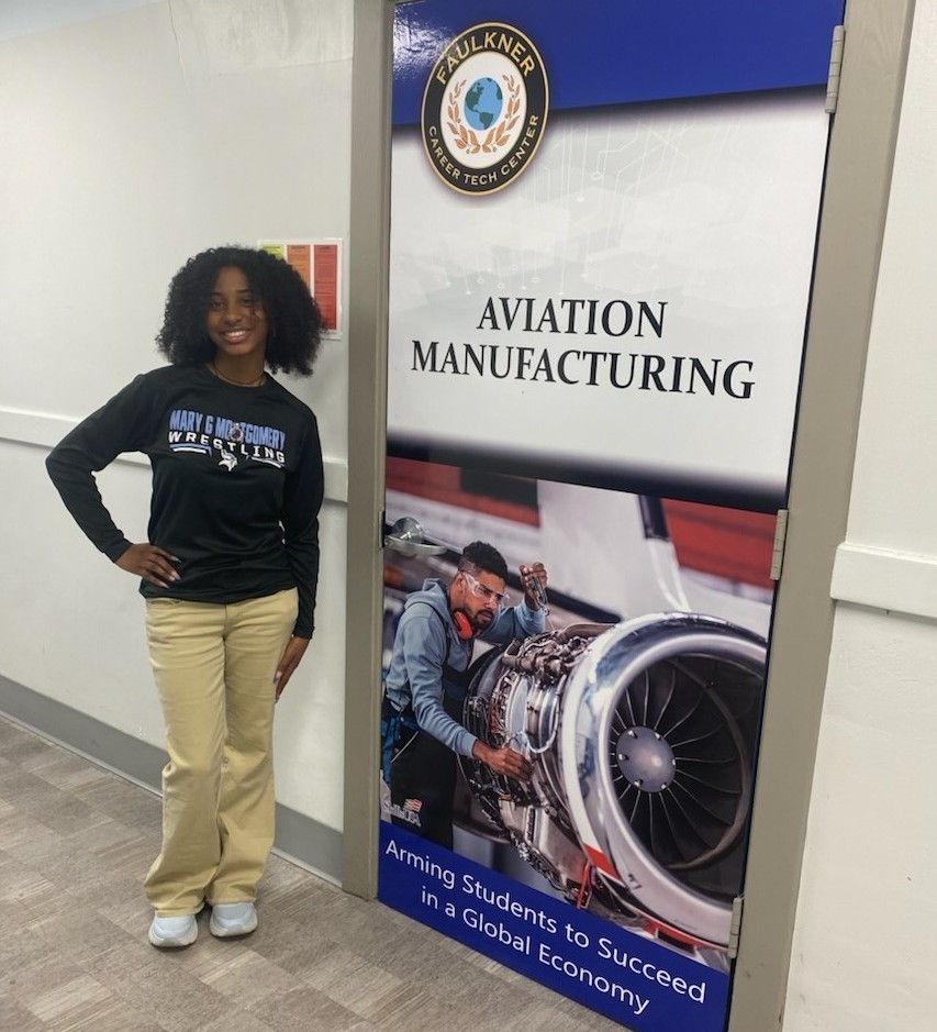 A high school girl stands next to a poster for Aviation Manufacturing