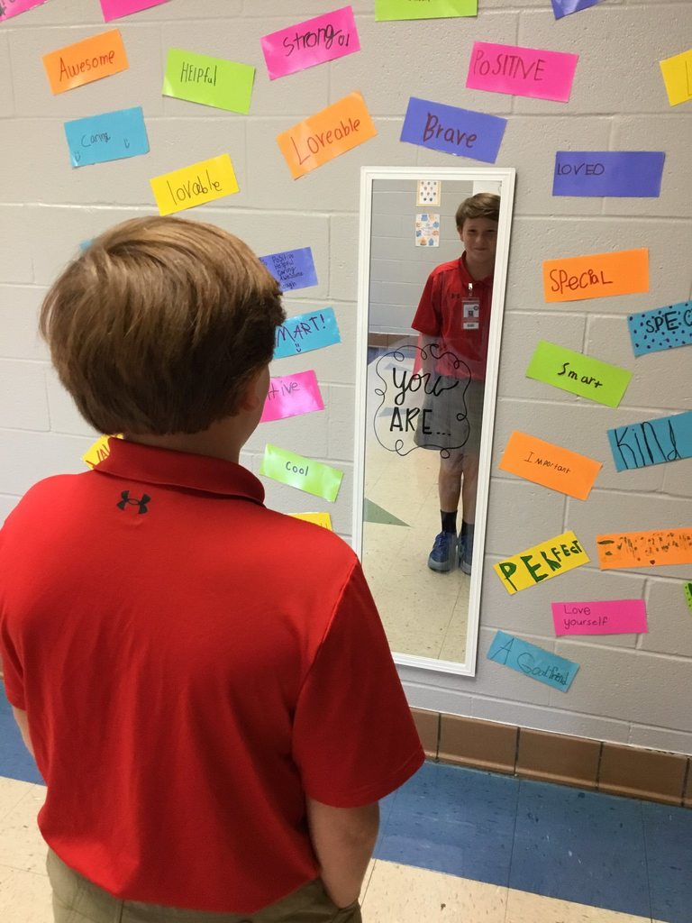 A boy looking into a mirror with notes of positive affirmation around it