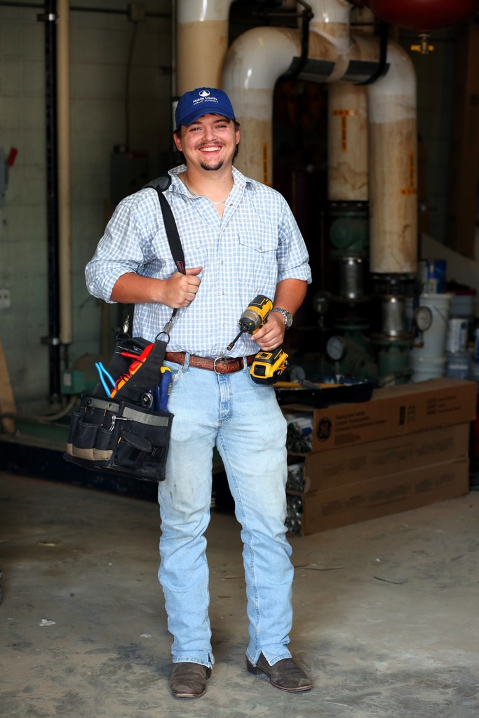 A man in jeans and a cap holding a drill and a tool bag
