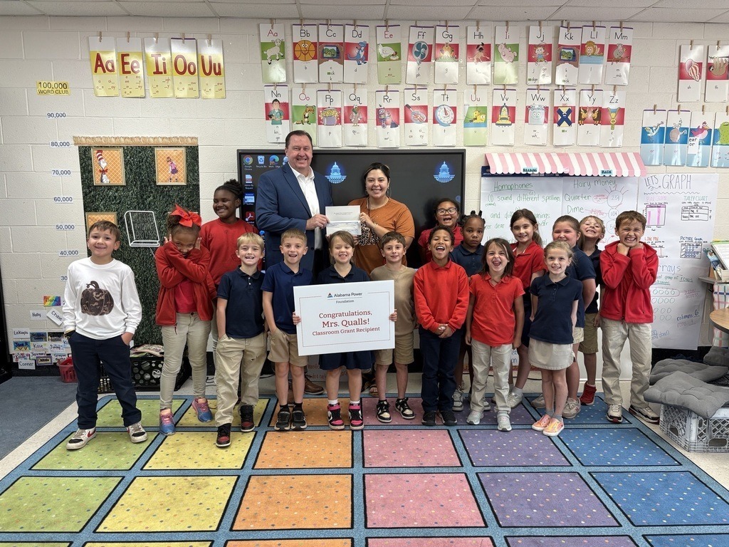 A teacher in a classroom with a group of students and a representive of Alabama Power Company